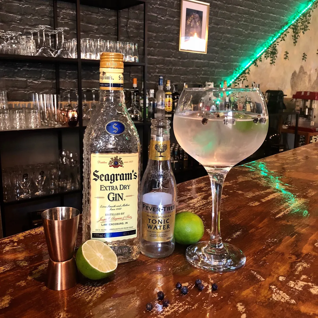 Gin-tonic en copa con lima junto a la botella de ginebra